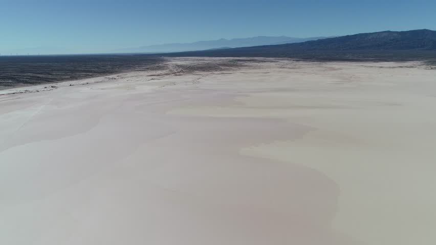 Aerial drone scene of barreal desert at aimogasta, la rioja, argentina. Camera moving backwards and discovering small adobe houses. The andes mountains on background. Car tracks on the field.
