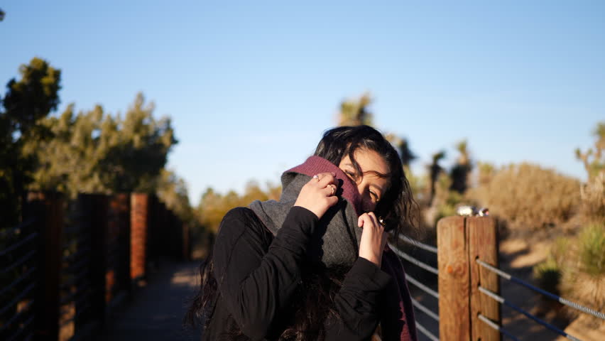 A pretty girl with long black hair and a scarf smiling and laughing hard in a shy cute way.