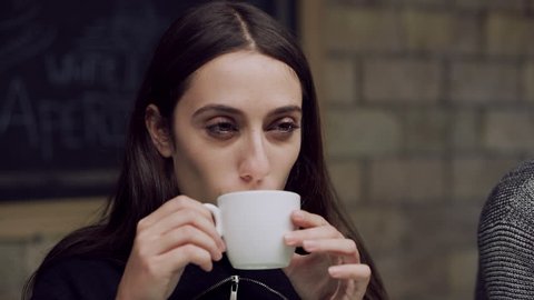 In a small Italian cafe, a thoughtful woman sits and drinks her coffee from a white cup. Close up shot on 8k RED camera.