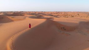 Woman walking in the desert during sunset aerial view
