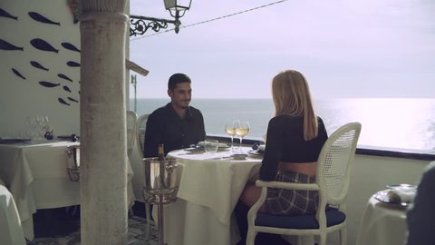 At a table overlooking the ocean, a loving couple hold hands while enjoying the view in the Amalfi Coast. Medium shot on 8k helium RED camera.
