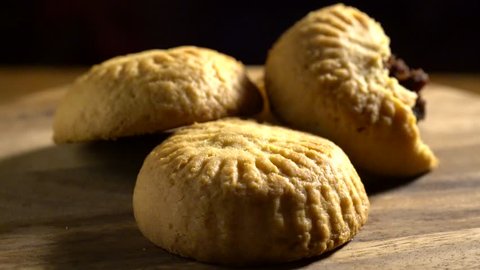 Closeup of three maamoul, arabic cookies with one broken open to see the date filling, rotating slowly in pretty light with black background.