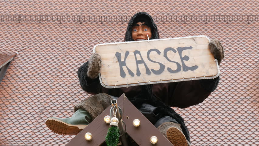 Funny moving doll sits on a Christmas stand and holds in his hand a sign that says Cashier in German