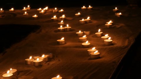 A large number of small white round candles burning in the sand. Background of burning wax candles