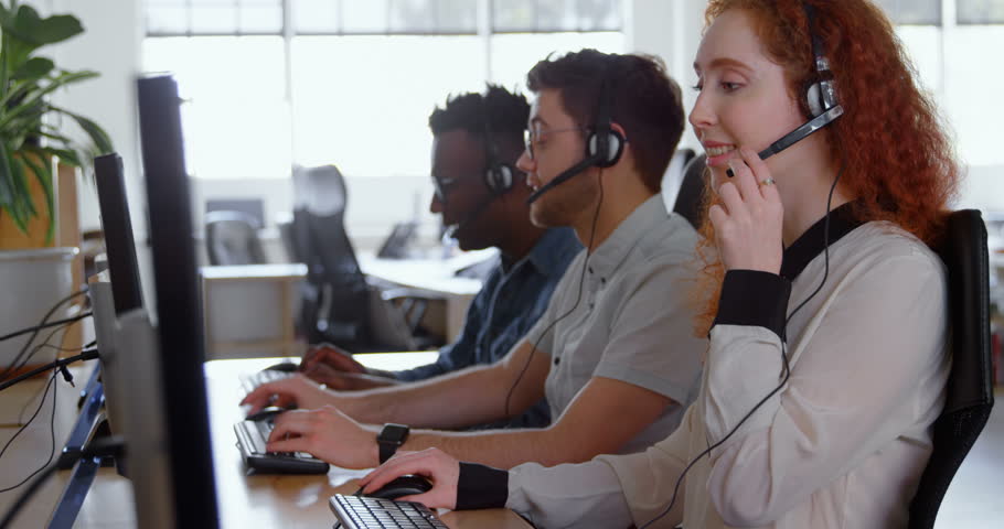 Side view of young cool diverse call center team calling and sitting at desk of modern office. They are using desktop pc and interacting with customer. | Shutterstock HD Video #1023986102