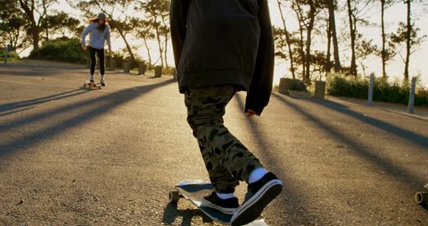 Rear view of young Caucasian skateboarder riding on skateboard on country road. Skateboarders skating together in the sunshine  库存视频