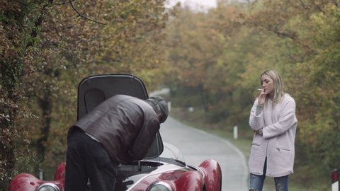 An impatient woman waits as her boyfriend fixes a vintage car on the side of a quiet street in rural Tuscany. Wide shot on 8k helium RED Camera.