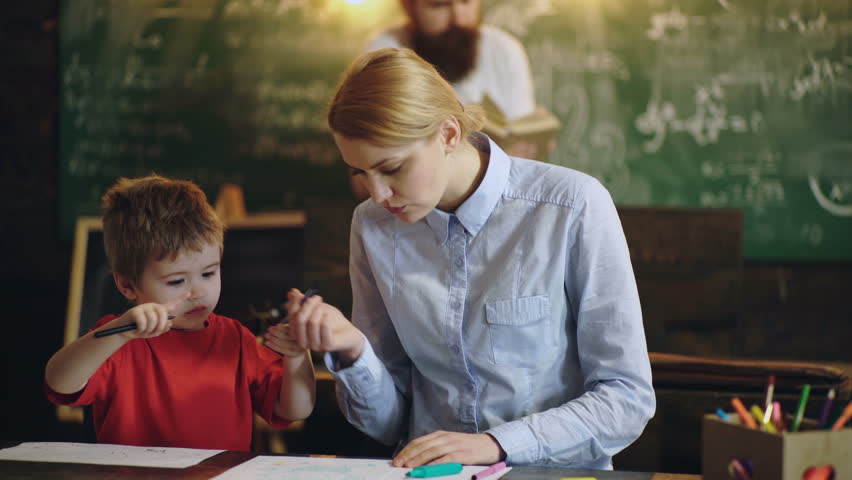 Woman with a boy is painted at the table against the background of a bearded man who reads a book. Learning concept. Back to school. Parents draw with their son in a school class