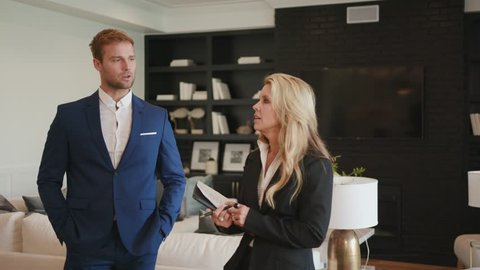Realtor woman 50s showing a property to young businessman at open house / Selling Real estate 