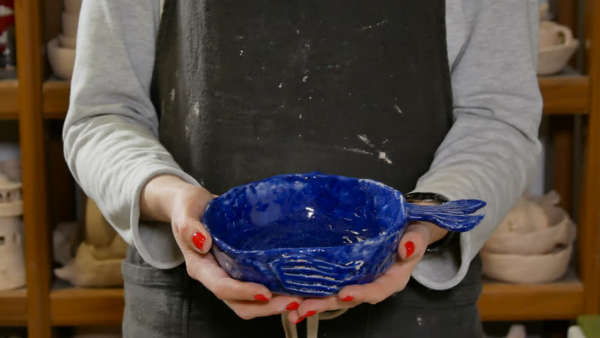 Creative ceramist glazed shows burned earthenware bowl, piece ready for use, close-up female potter hands, person unrecognisable