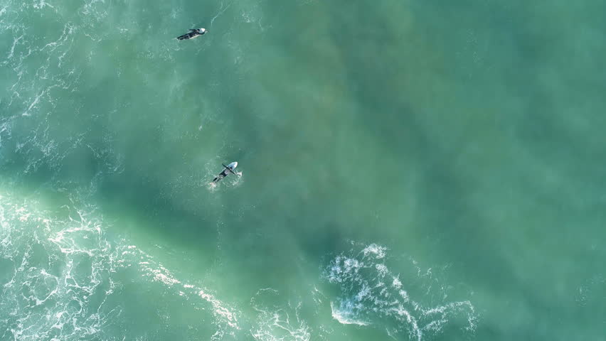 Two surfers with surfing boards swimming and waiting a wave in blue turquoise ocean. Aerial cinematic drone shot