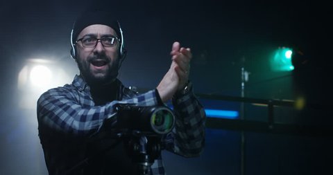 Medium shot of young director giving instructions on a film set while holding an equipment shot on RED camera.