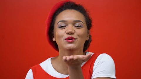 Funny african american woman sending air kisses, isolated red background, love