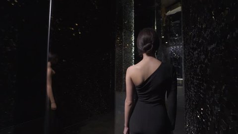 BELARUS, MINSK - AUGUST 17, 2017: Back view of elegant woman in a black dress walking to meet in modern restaurant, slow motion shooting.