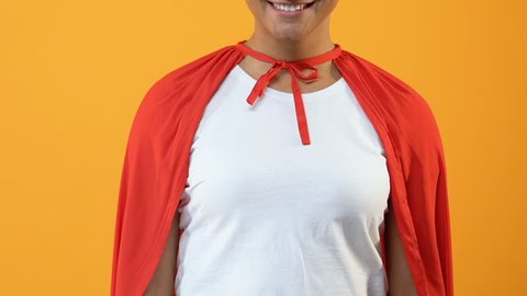 Smiling young lady in red cape on bright background, powerful wonder woman