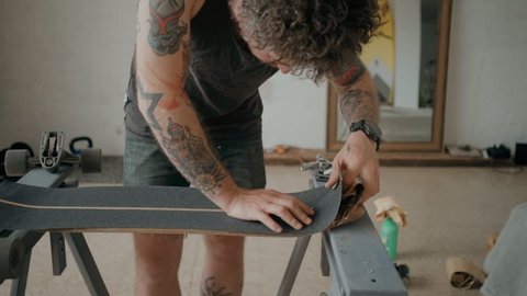 Soft focus beautiful cinematic shot of urban skateboarder or millennial hipster in designer loft studio or wokshop, work on regripping old skateboard and attaching new tape. Concept diy Stock Video