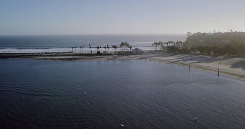 Aerial footage of ocean point an crashing waves at the beach in southern California near Long Beach and Los Angeles at sunset with Palm Trees.