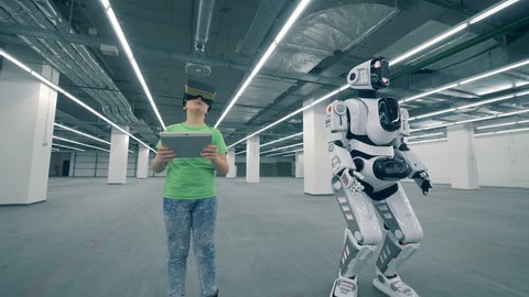 Empty storage unit with a boy in VR-glasses and a moving robot – Stockvideo
