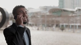 Smiling young man having conversation through modern phone outdoor.