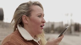 Mature woman wearing warm clothing talking on smartphone outdoor.
