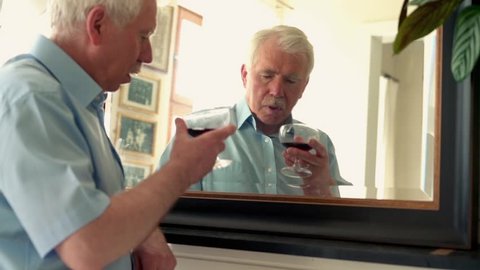 Senior drunk man drinking wine in front of the mirror
