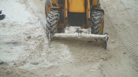 Tractor shoveling snow on the street. Slow-motion.