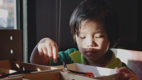 Little Asian baby girl, 36 months old, enjoys eating tomato sauce on a piece of pizza by hand and fork by herself at a restaurant