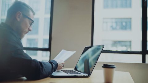 Bearded businessman man working at sunny office on desktop computer while sitting at wooden table.