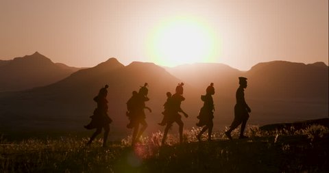 4K view of people from the Himba tribe in traditional dress, walking along a path with scenic mountains in the background, Namib desert, Namibia