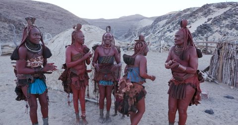 4K view of Himba woman in traditional dress dancing and singing outside their clay hut, Namibia