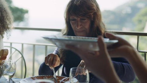 Happy Italian woman eating a plate of vegetables at a table outside with his friends and family, Amalfi Coast. Close up shot on 8k helium RED camera.