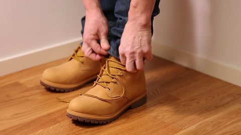 Man in jeans putting on and tying yellow shoes. People backgrounds.