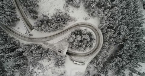 Stationary birds eye view shot of car driving along snow covered mountain road