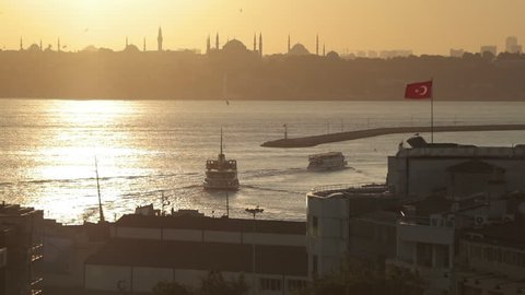 Istanbul bosphorus panoramic view during sunset time. Hagia Sophia and Sultanahmet mosque appear in the background. Ferries and ships passing. There is a Turkish Flag.