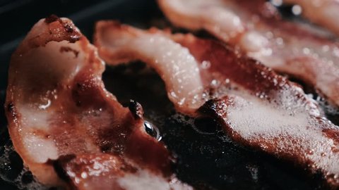 Closeup panning shot of bacon strips frying on a pan. Closeup, panning shot of bacon strips frying to a crisp on a frying pan.