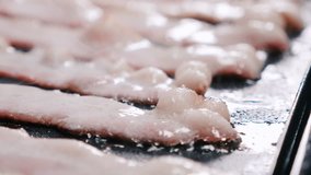 A clip showing uncooked, raw bacon pieces over oil on a frying pan. The video slowly moves on a clockwise direction.