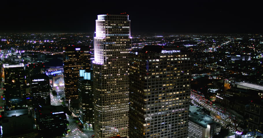 Sexy aerial wide shot of downtown Los Angeles skyscrapers at night showing city lights and building towers from a helicopter point of view with urban streets and traffic.