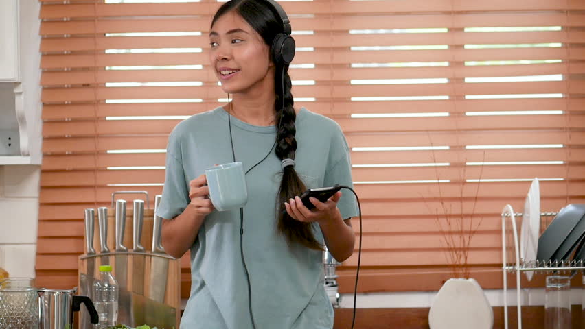 Young asian woman using mobile phone at home and drinking coffee.