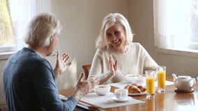 Happy senior older couple talking laughing having healthy morning breakfast and fun conversation together, loving mature middle aged family eat meal together sitting at kitchen dining table at home - Powered by Shutterstock - Get 15% off with code: PIKWIZARD15
