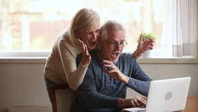 Excited happy senior old family couple winners using laptop overjoyed by unbelievable online betting bid playing internet casino game lottery win screaming with joy looking at computer screen