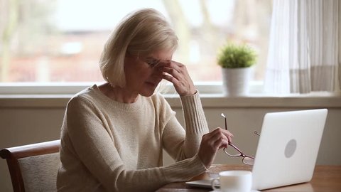 Senior woman using laptop feeling discomfort from dry irritated fatigued eyes taking off glasses, older mature businesswoman tired of computer worker suffering from blurry vision eyestrain problem