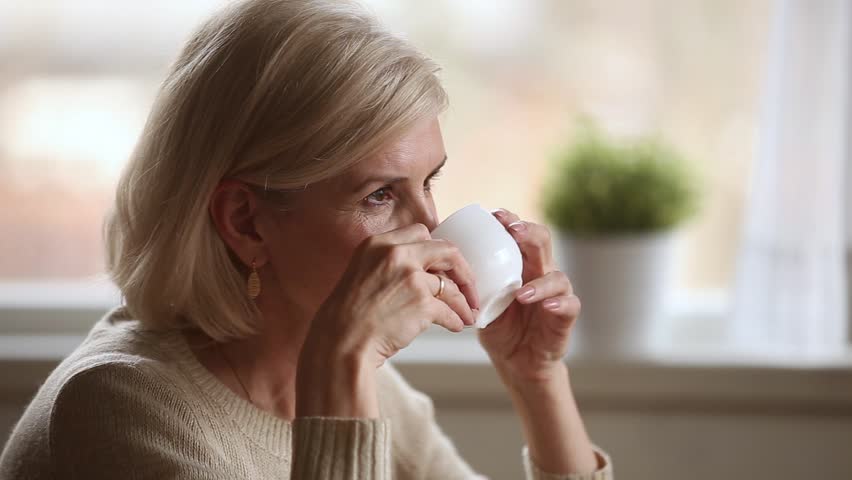 Dreamy happy middle aged mature woman looking away drinking morning coffee or tea at home, smiling senior old lady holding cup relaxing with positive thoughts dreaming enjoying pleasant memories Royalty-Free Stock Footage #1024093994