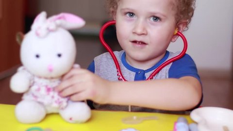 Little boy plays doctor: treats a teddy rabbit
