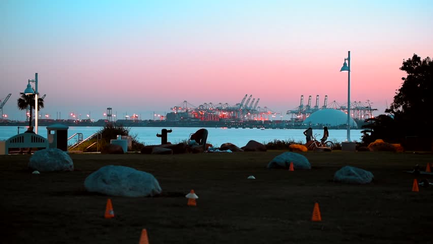 Park scene in Long Beach California as the sunsets with people in silhouette standing and riding scooters.