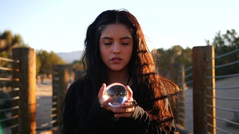 A beautiful woman with magic powers looking serious and staring into her magical crystal ball while casting an enchanting spell to predict the future. Video de stock