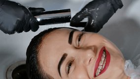 Happy woman with braces relax washing hair from color dyeing. Professional hairdresser use shampoo. Hair care and beauty studio business