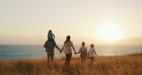 Happy family walking in golden field and looking out to the sunset together by the ocean