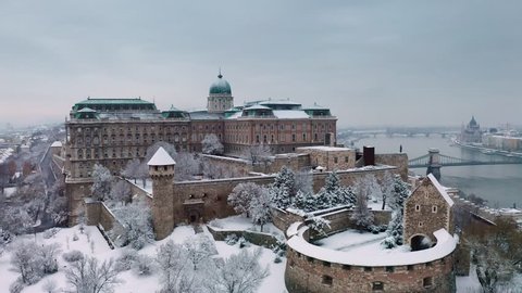 Budapest, Hungary - 4K flying up on a snowy winter morning at Buda Castle Royal Palace with Szechenyi Chain Bridge and Parliament at background