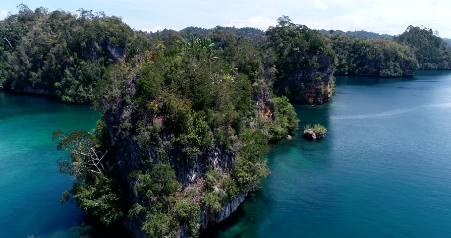 Drone footage of Raja Ampat, Indonesia with a liveaboard boat along karst islands covered in tropical vegtation in the south of Waigeo island near the passage with Gam island. The camera is facing sma
