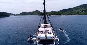Drone footage of Raja Ampat, Indonesia with a liveaboard boat anchored near Janggelo or Yanggelo island, two zodiacs with divers are going over turquoise water and shallow coral reef. 